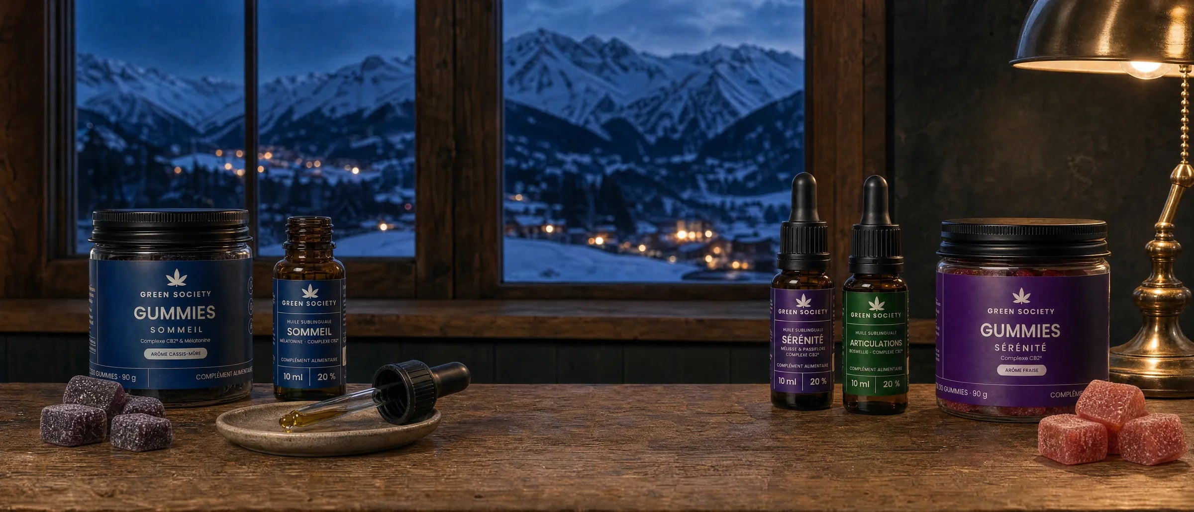 Gamme bien-être Green Society : huiles et gummies au Complexe CB2 sur un comptoir de chalet, face aux montagnes à la tombée du jour